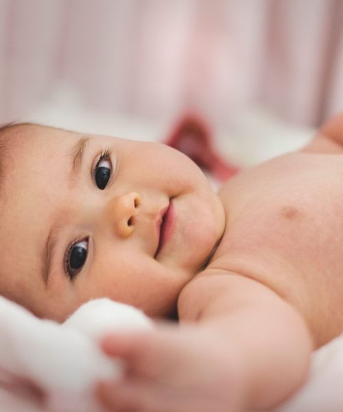 Cute baby lying on a soft bed, expressing innocence and joy in a cozy indoor setting.