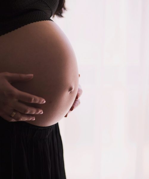 A close-up of a pregnant woman touching her bare belly, expressing warmth and care.